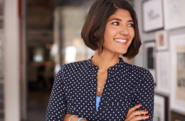 Woman in a blue and white dotted blouse with brown short hair smiling with her arms crossed.