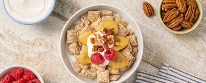 Bananas Foster in a white bowl on a wooden countertop with walnuts and raspberries around it.