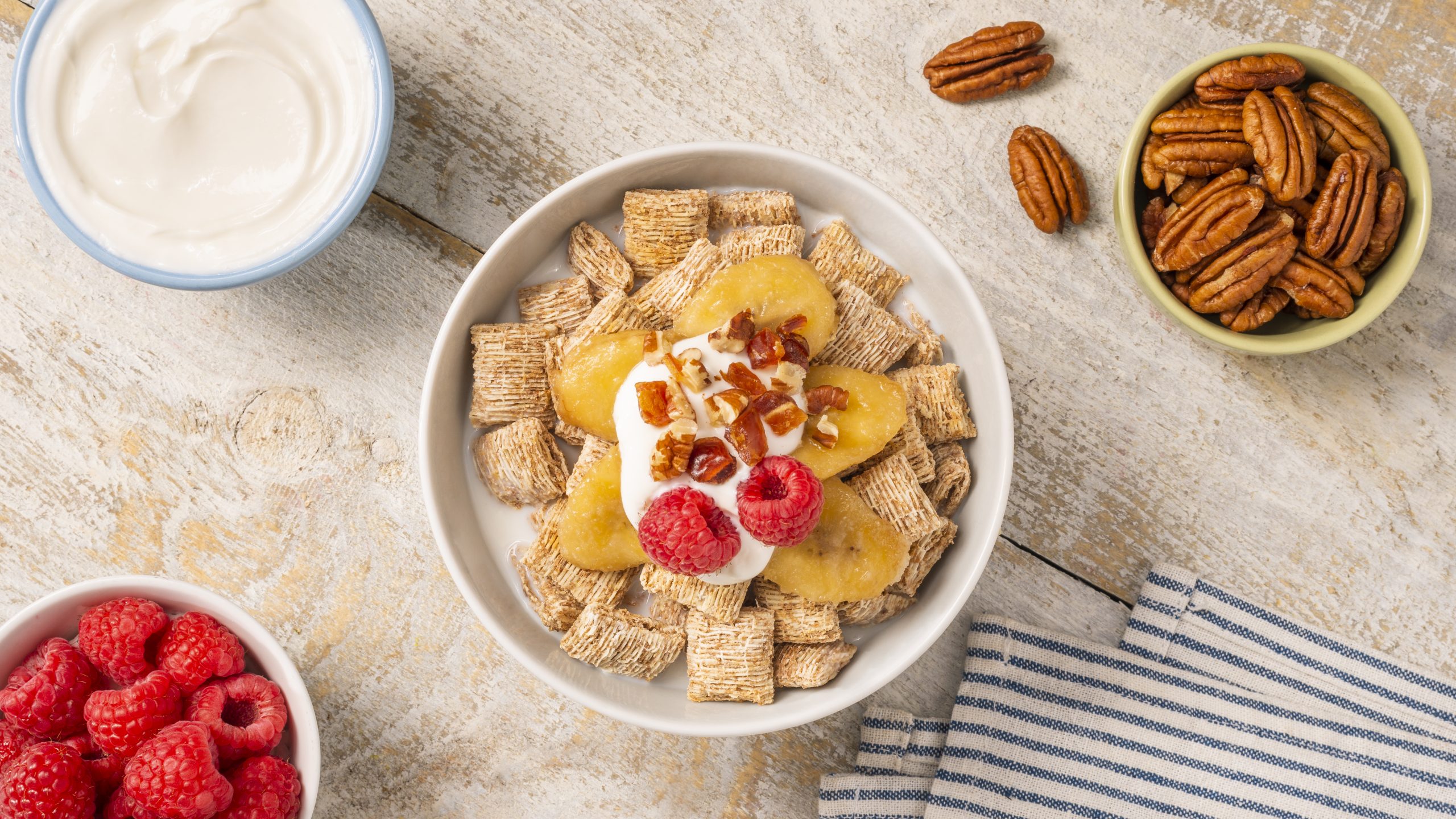 Bananas Foster in a white bowl on a wooden countertop with walnuts and raspberries around it.