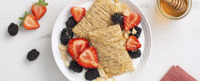 Shredded Wheat biscuits in a bowl with honey, strawberries and blackberries on top.