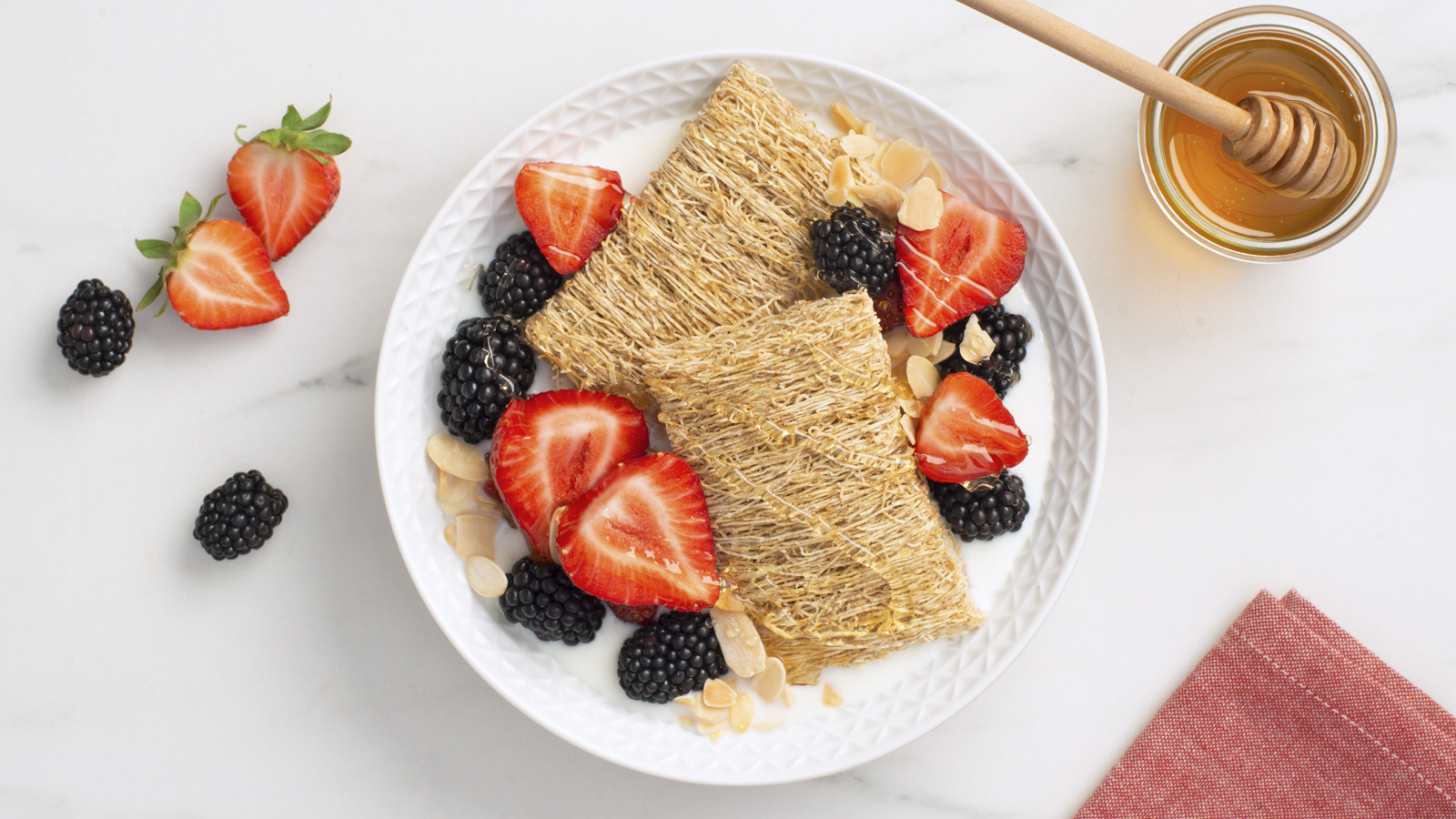 Shredded Wheat biscuits in a bowl with honey, strawberries and blackberries on top.