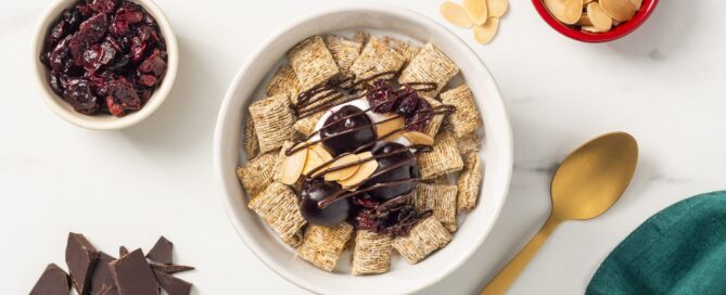 Spoon Sized Shredded Wheat in a bowl with cherries, yogurt and chocolate drizzle on top.