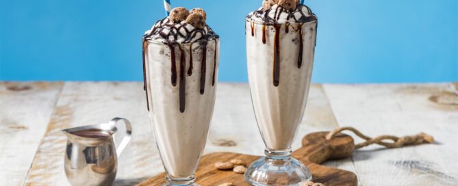 Two Chips Ahoy Cereal Milkshakes in tall cups with chocolate garnish and  blue and white straws.