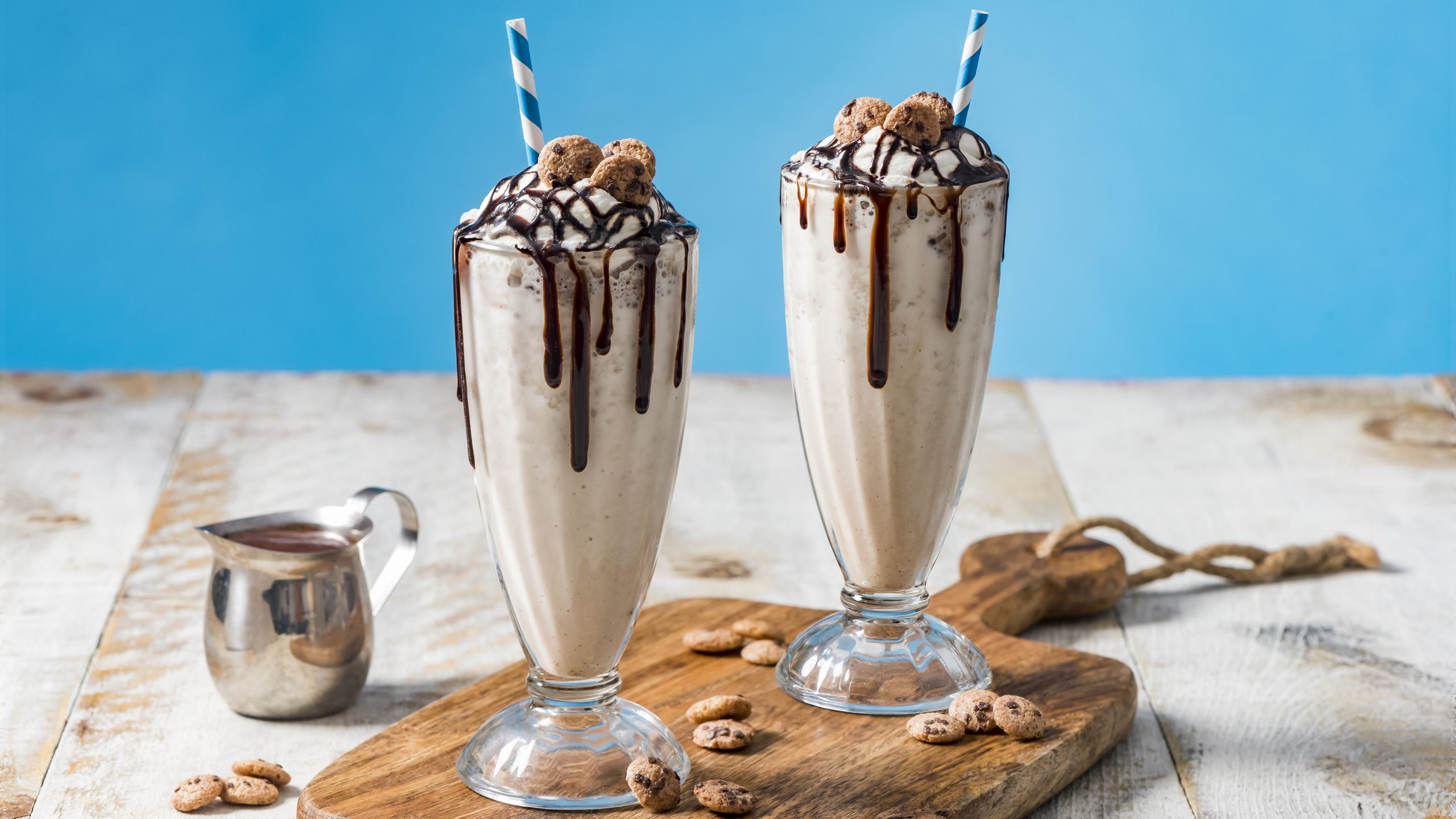 Two Chips Ahoy Cereal Milkshakes in tall cups with chocolate garnish and  blue and white straws.