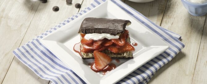 Chocolate Maple Strawberry Shredded Wheat Sandwich on a white plate with strawberries and whipped cream in a bowl in the background.
