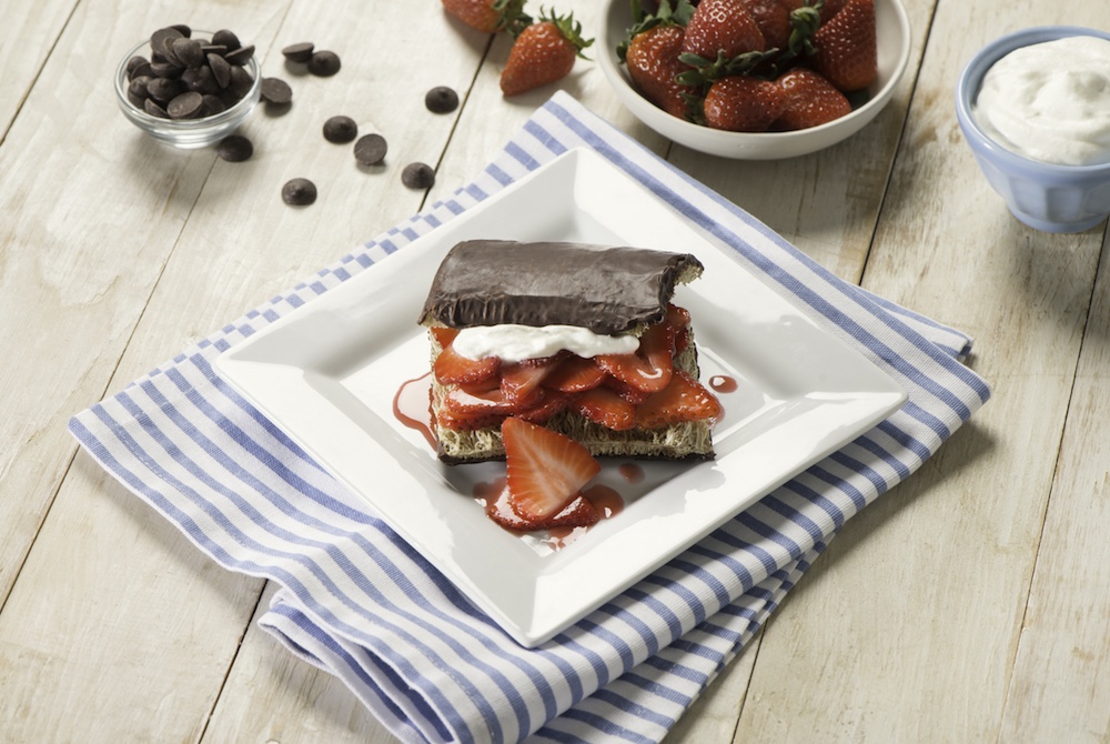 Chocolate Maple Strawberry Shredded Wheat Sandwich on a white plate with strawberries and whipped cream in a bowl in the background. 