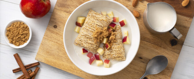Biscuits au blé râpé dans un bol de lait avec de la cannelle et des pommes dessus.