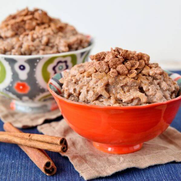 Cocoa pebbled rice pudding in a red bowl with cinnamon sticks