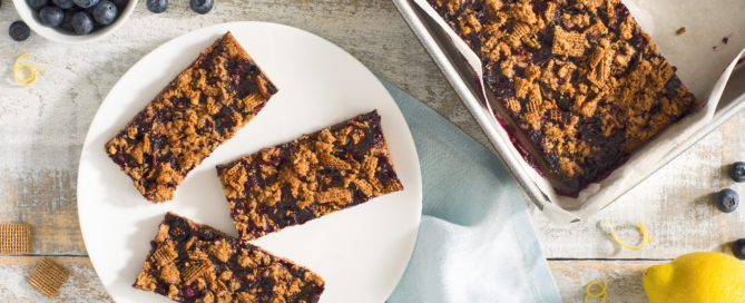 Shreddies Blueberry Crumble Bar on a white plate with a bowl of blueberries and a lemon on the side.