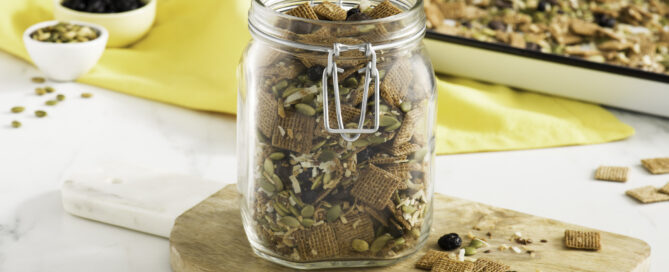 Shreddies Crunchy Superfoods Snack Mix in a mason jar on a wooden cutting board.