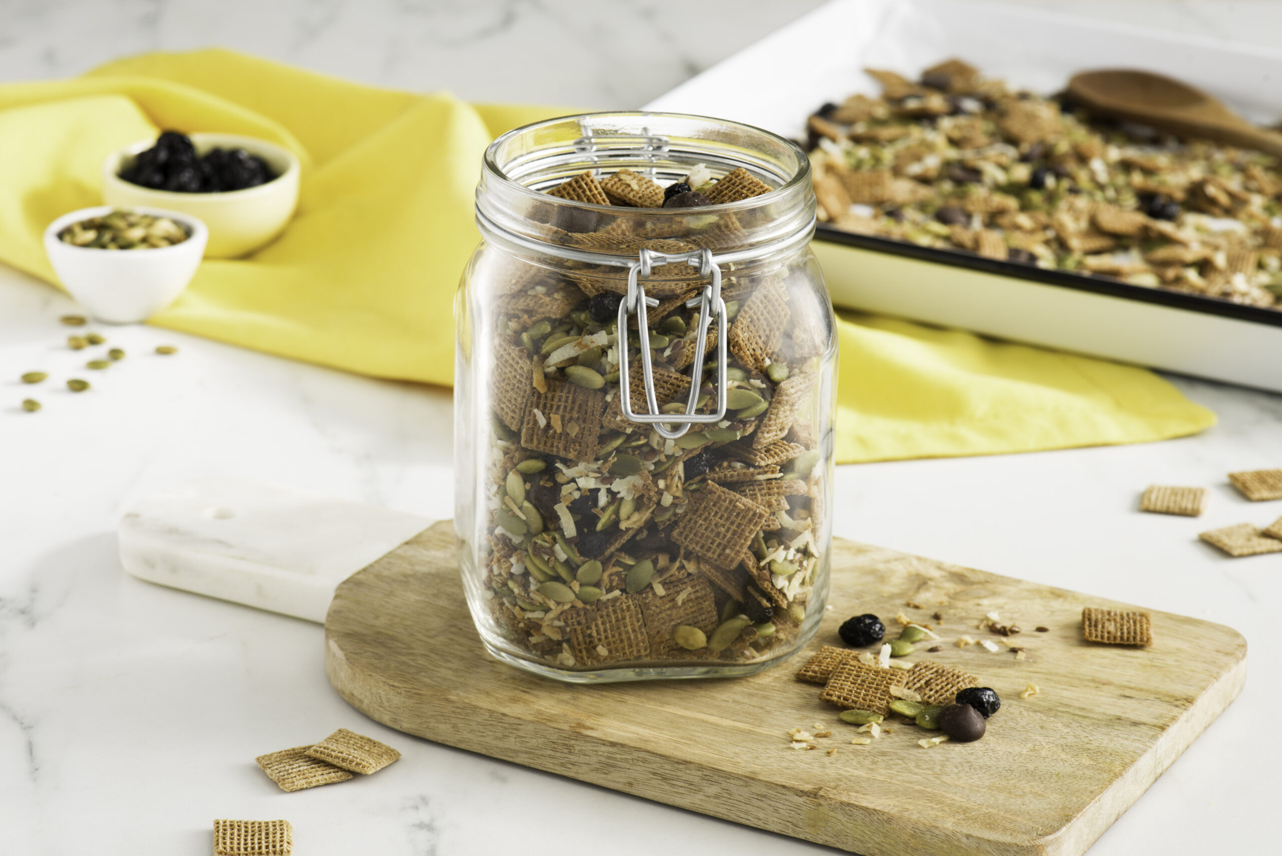 Shreddies Crunchy Superfoods Snack Mix in a mason jar on a wooden cutting board.