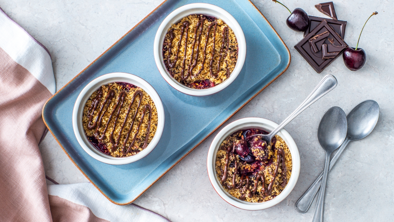 Dark Chocolate and Cherry Shredded Wheat Crumbs in white bowls with dark chocolate pieces and cherries on the side.