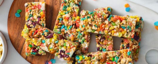 Fruity pebbles granola bars on a white and wooden cutting board.