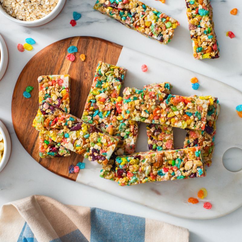 Fruity pebbles granola bars on a white and wooden cutting board.