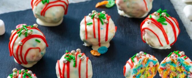 Fruity pebbles holiday truffles on a black stone with cereal pieces scattered about in the background.
