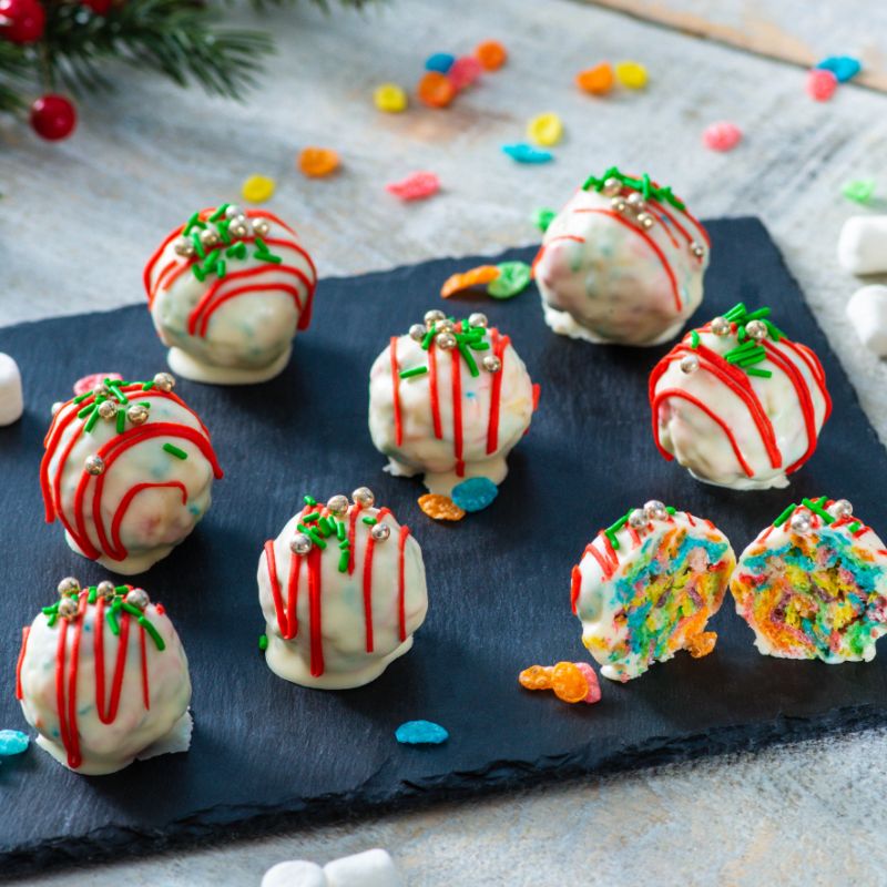 Fruity pebbles holiday truffles on a black stone with cereal pieces scattered about in the background.