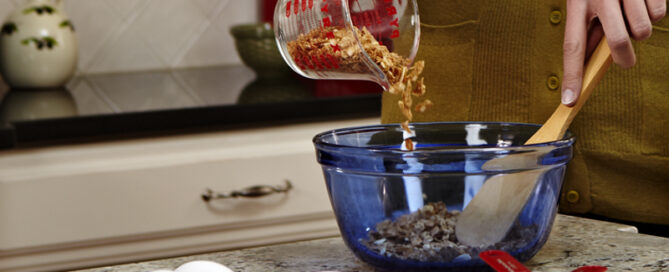 A woman mixing oats in a blue mixing bowl with a wooden spoon.