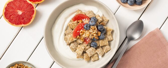 Shredded Wheat Grapefruit Omega in a white bowl with a spoon and sliced grapefruit on the side.