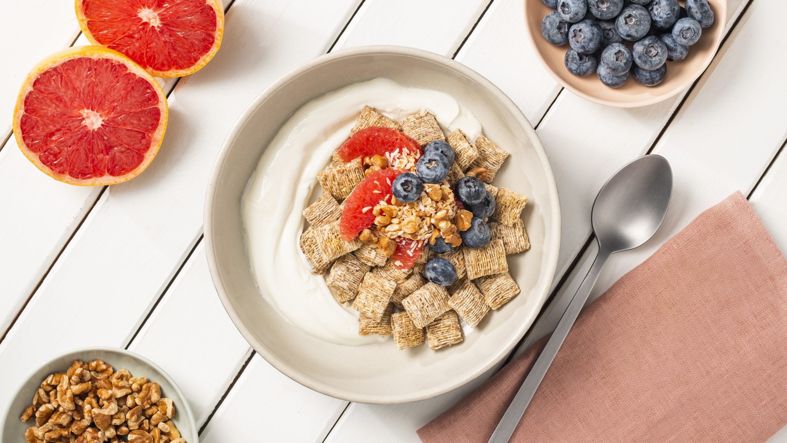 Shredded Wheat Grapefruit Omega in a white bowl with a spoon and sliced grapefruit on the side.