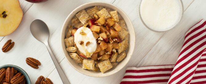 Hot Apple Crumble made with Shredded Wheat in a white bowl with pecans and a spoon on the side.
