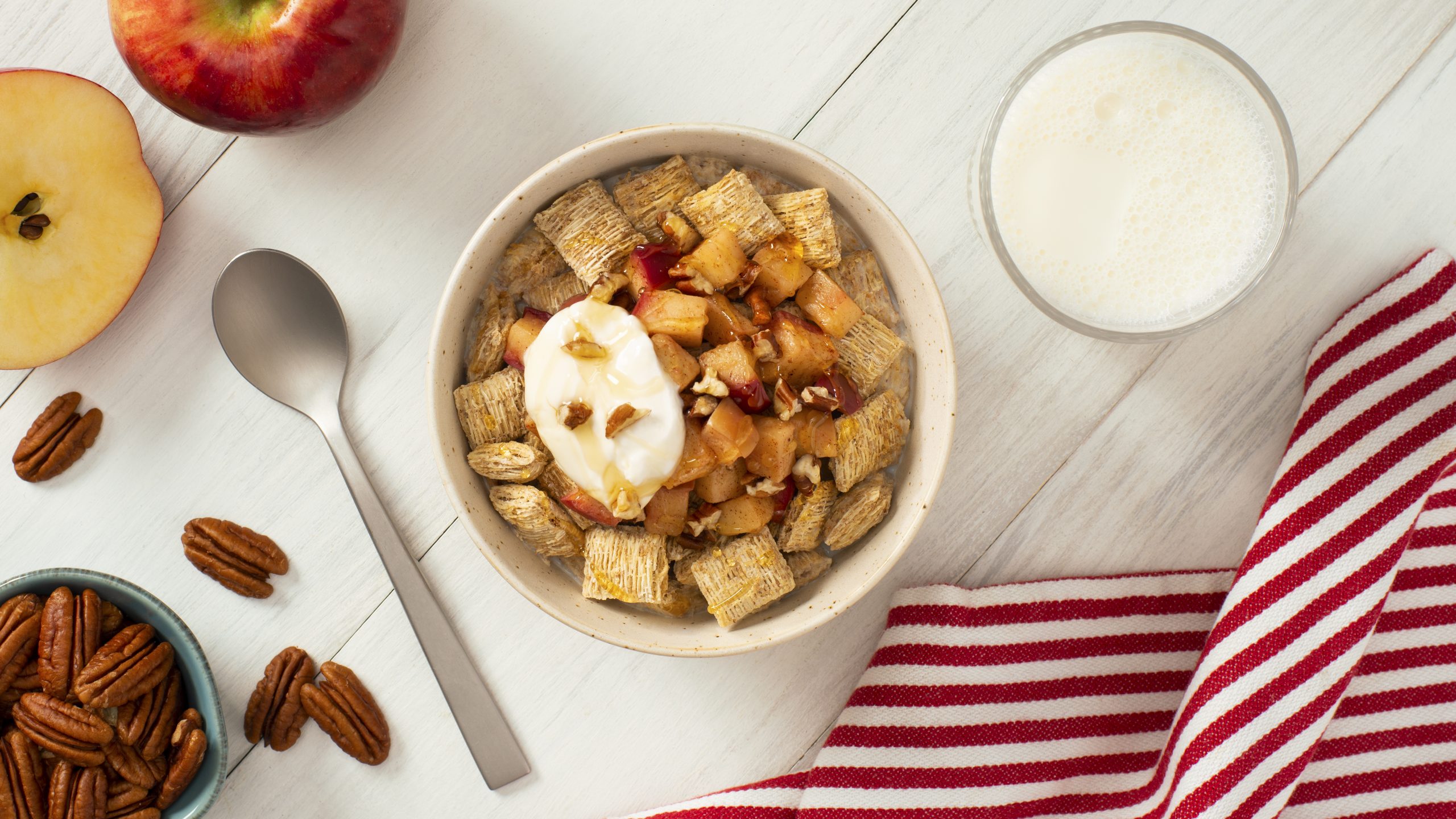 Hot Apple Crumble made with Shredded Wheat in a white bowl with pecans and a spoon on the side.