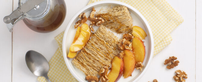 Two shredded wheat biscuits in a white bowl with peaches and honey on top.