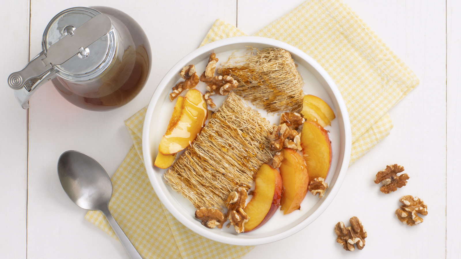 Two shredded wheat biscuits in a white bowl with peaches and honey on top.