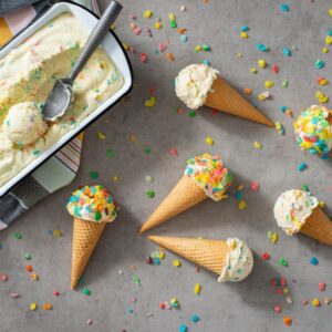 Fruity pebbles cereal no-churn ice cream cones sitting on a grey tabletop with cereal scattered about.
