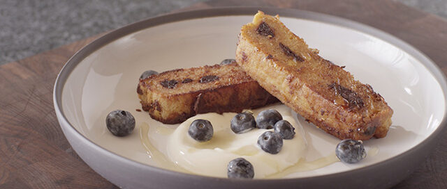 French Toast with Anicet Honey Yogurt and Dried Blueberries in a white bowl with honey on top.
