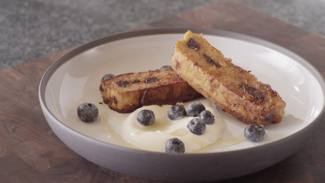 French Toast with Anicet Honey Yogurt and Dried Blueberries in a white bowl with honey on top.