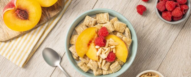 Shredded Wheat spoon size in a blue bowl with sliced peaches and raspberries on top.