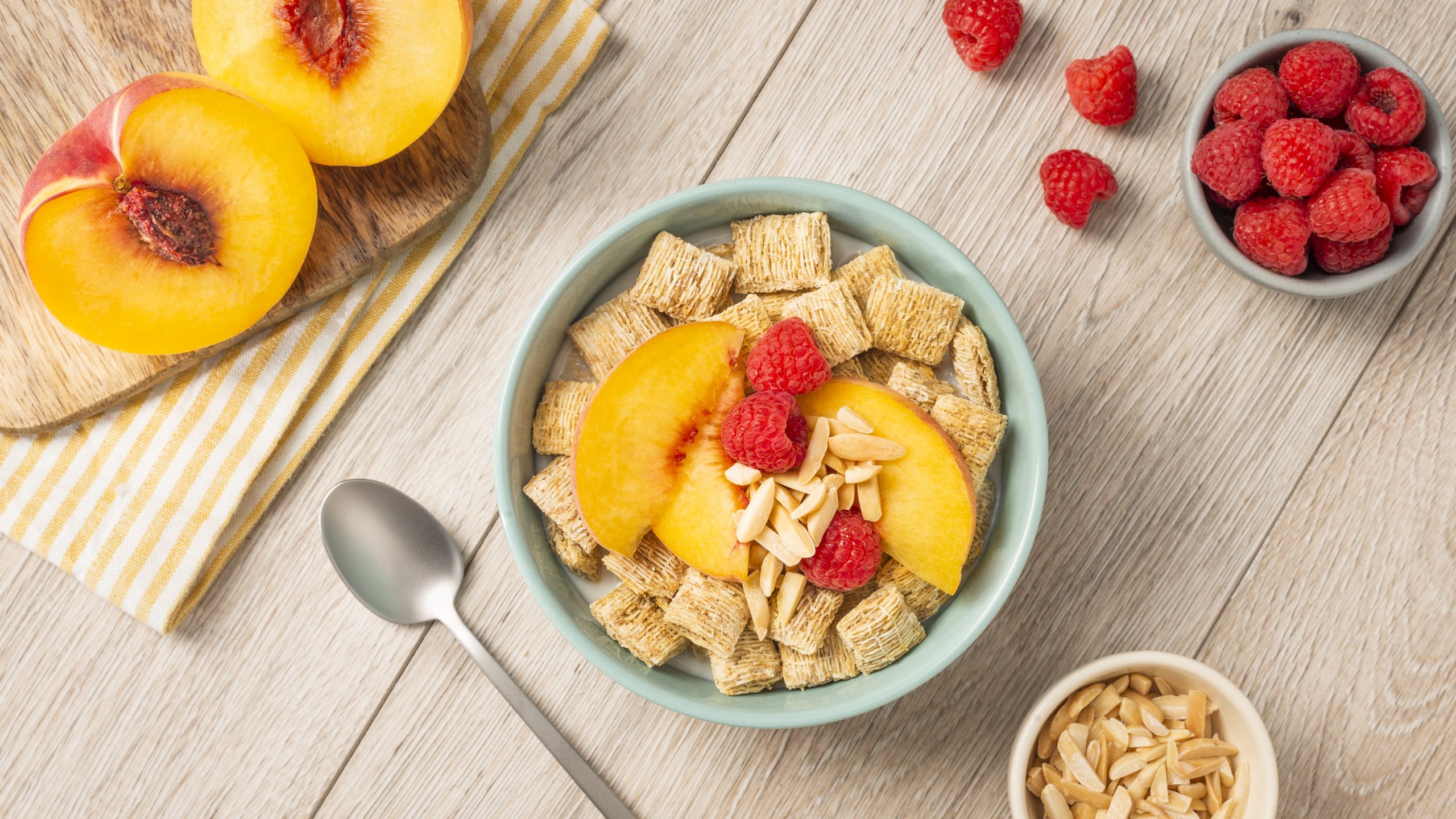 Shredded Wheat spoon size in a blue bowl with sliced peaches and raspberries on top.