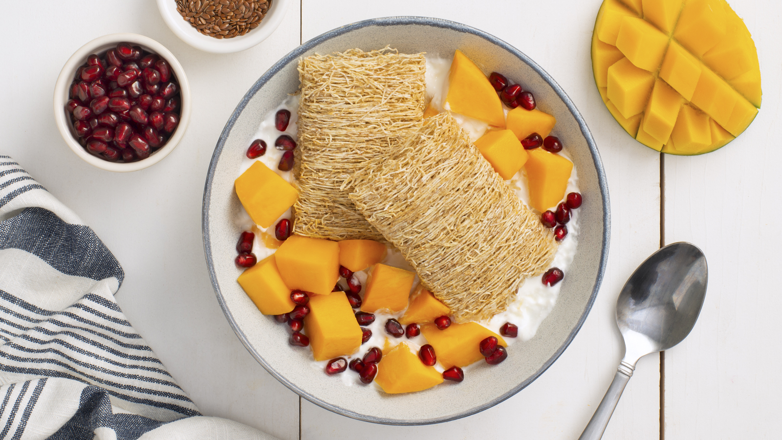 Two Shredded Wheat biscuits in a white bowl with mango pieces and pomegranate pieces.