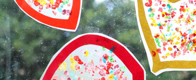 Stained glass paper craft on a window with green foliage in the background.