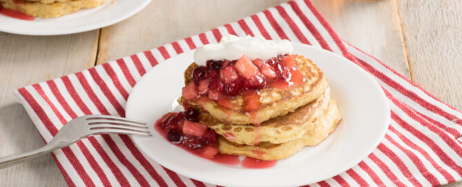Shredded Wheat Pancakes on a white plate with sliced strawberries and maple syrup on top.
