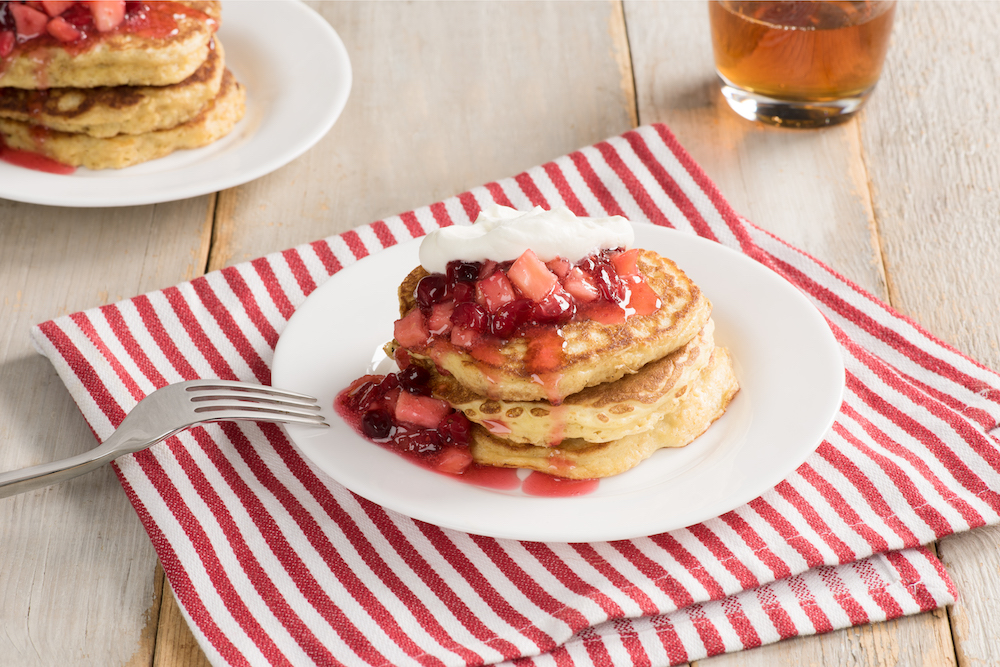 Shredded Wheat Pancakes on a white plate with sliced strawberries and maple syrup on top.