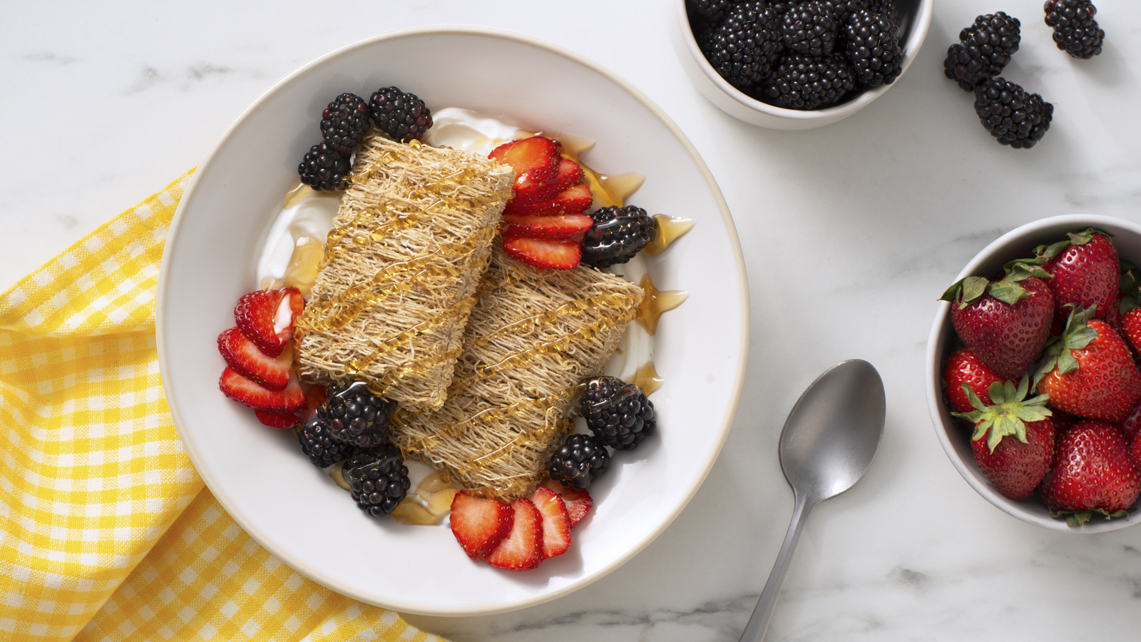 Shredded Wheat Very Berry Parfait in a white bowl with strawberries and blackberries on the side.