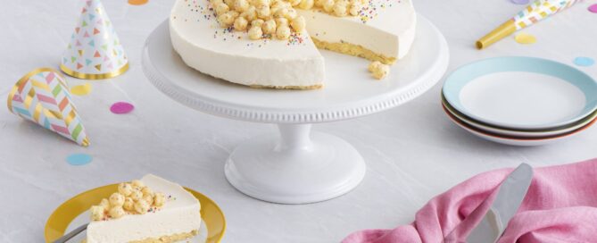 Timbits Birthday Cake cereal no bake cheesecake on a white platter with birthday hats and confetti in the background.