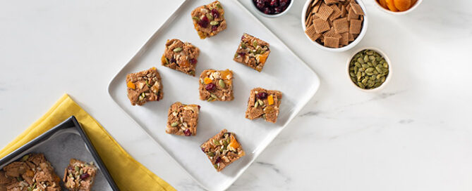 Trail Mix Shreddies Squares on a marble countertop with bowls of toppings on the side.