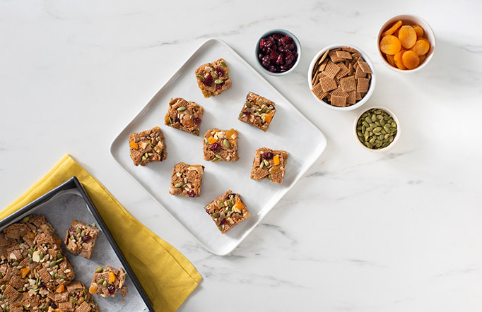 Trail Mix Shreddies Squares on a marble countertop with bowls of toppings on the side.
