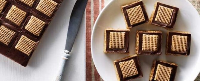 Shreddies Amazing No-Bake Peanut Butter Squares on a white plate with a red and brown table clothing in the background.