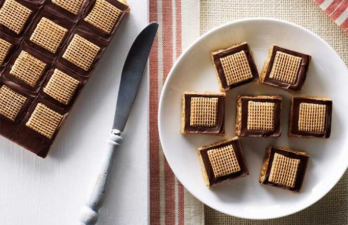 Shreddies Amazing No-Bake Peanut Butter Squares on a white plate with a red and brown table clothing in the background.