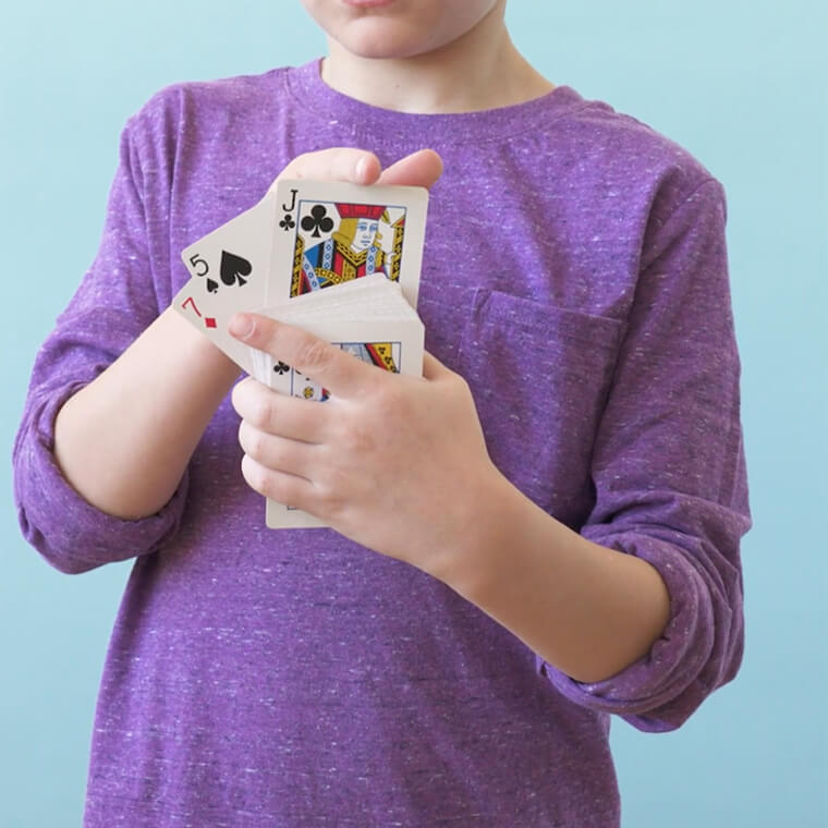 Child in a purple long sleeved shirt holding a deck of playing cards.