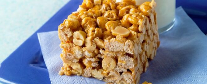 Chewy Caramel Bar sitting on a blue plate with a blue napkin and a glass of milk on the side.