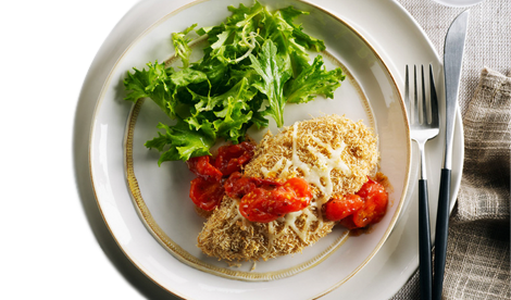 Chicken Parmesan on a white plate with tomatoes and lettuce on the side.