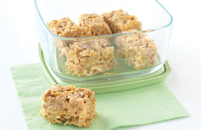 Trail mix cereal bars in a glass container on a green napkin.