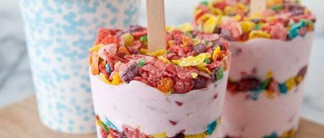 Fruity Pebbles yogurt popsicles sitting on a wooden cutting board.