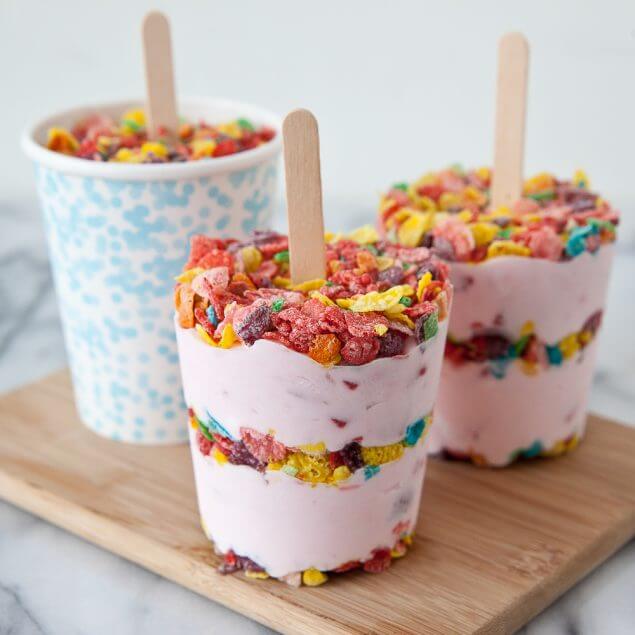 Fruity Pebbles yogurt popsicles sitting on a wooden cutting board.