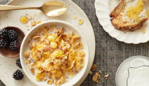 Honey Bunches of oats in a white bowl on a white plate with blackberries and honey.