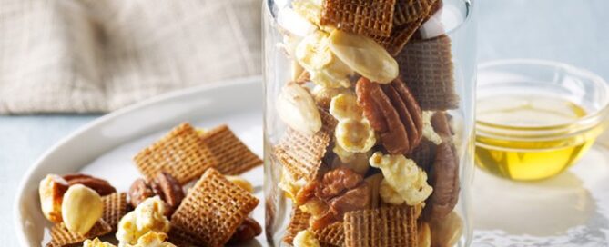 Shreddies Honey Nut Crunch Mix in a mason jar on a serving platter with a bowl of honey in the background.